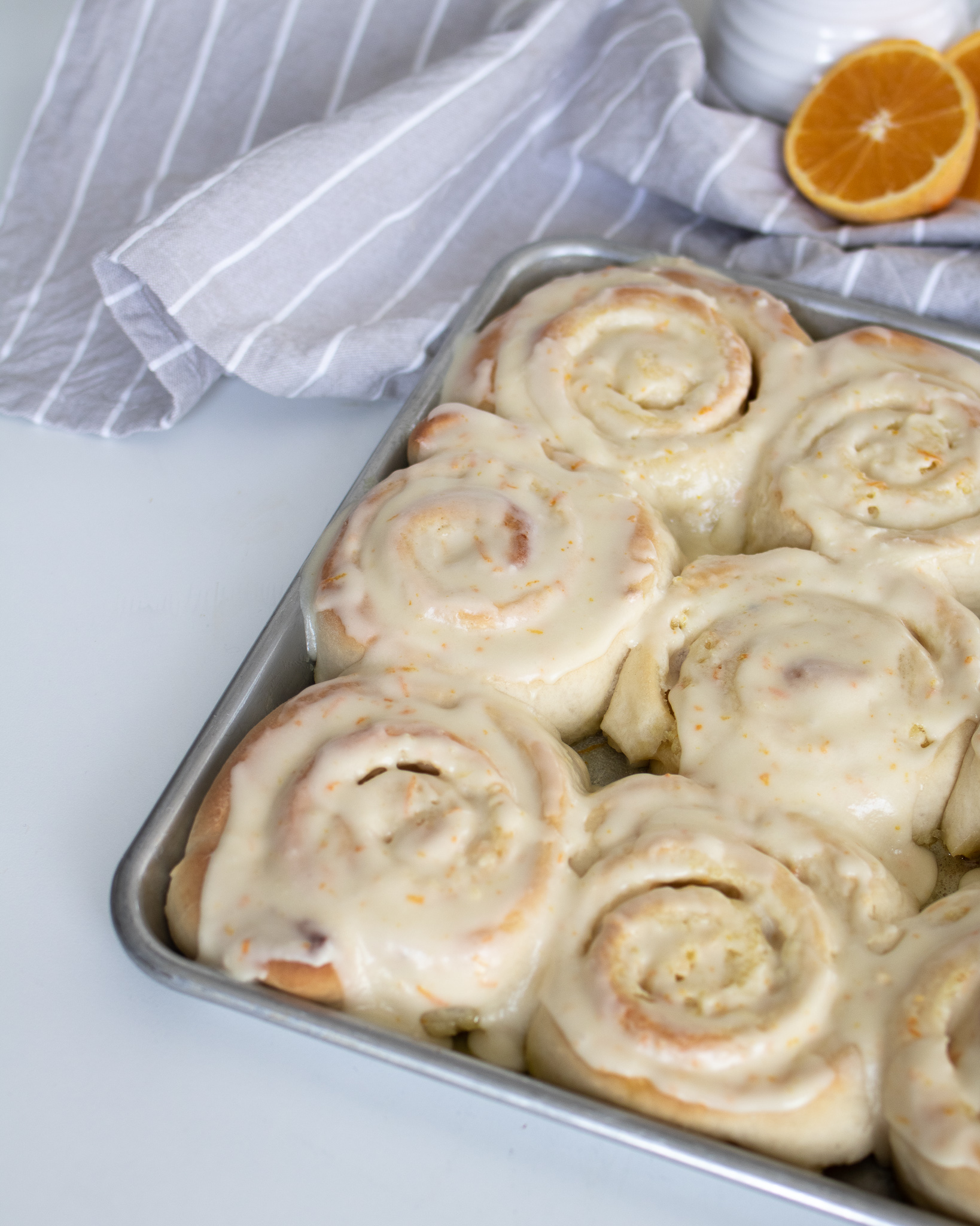 overhead view of cookie sheet full of frosted orange sweet rolls