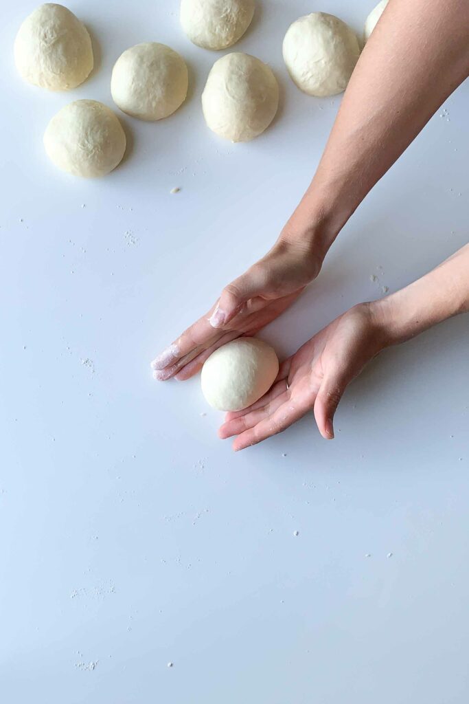 two hands shaping homemade dough into ball