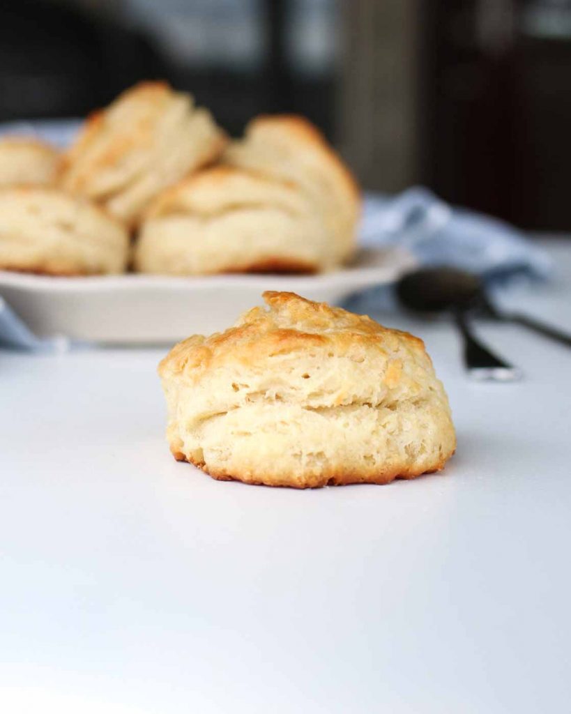 a single buttermilk biscuit with a bowl of buttermilk biscuits in the background