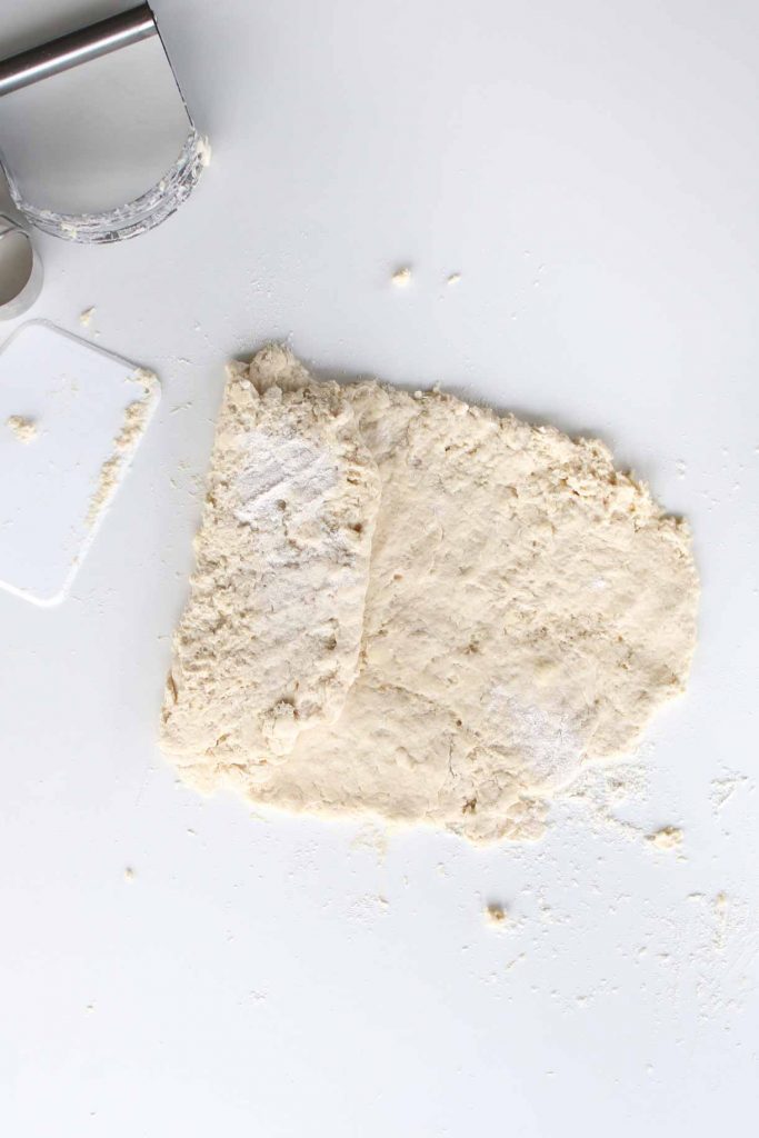 aerial view of folded biscuit dough, pastry cutter, biscuit cutter, and bench scraper
